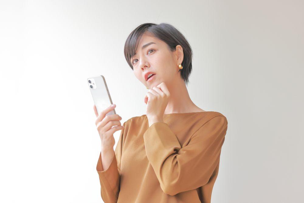 スマホを見ながら考える女性